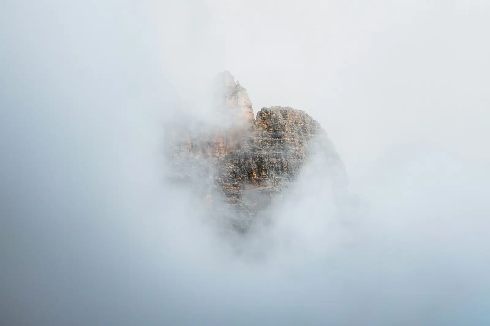 A rocky mountain peak partially obscured by thick white mist